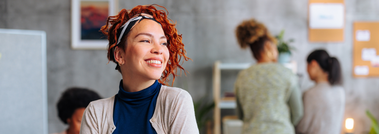 Multi-cultural women with ear and lip piercings smiles in an office setting.