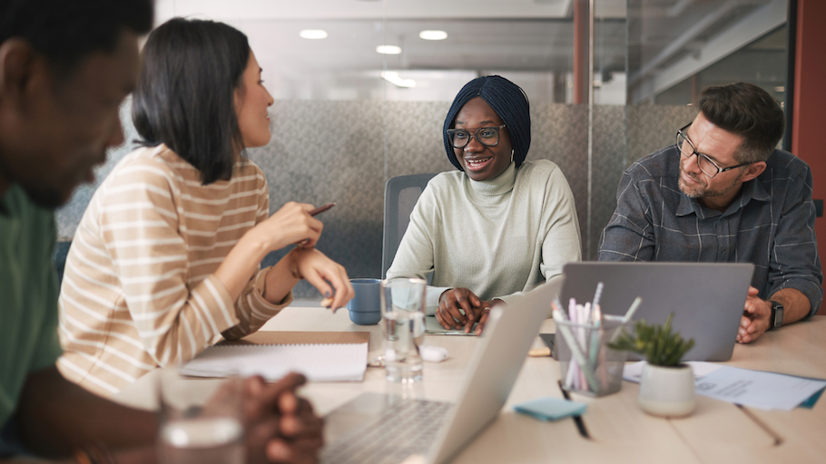 Four colleagues talking around a table that has laptops and papers on it