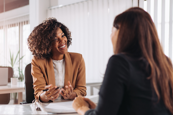 Two women sitting across from each other, one is smiling and explaining something